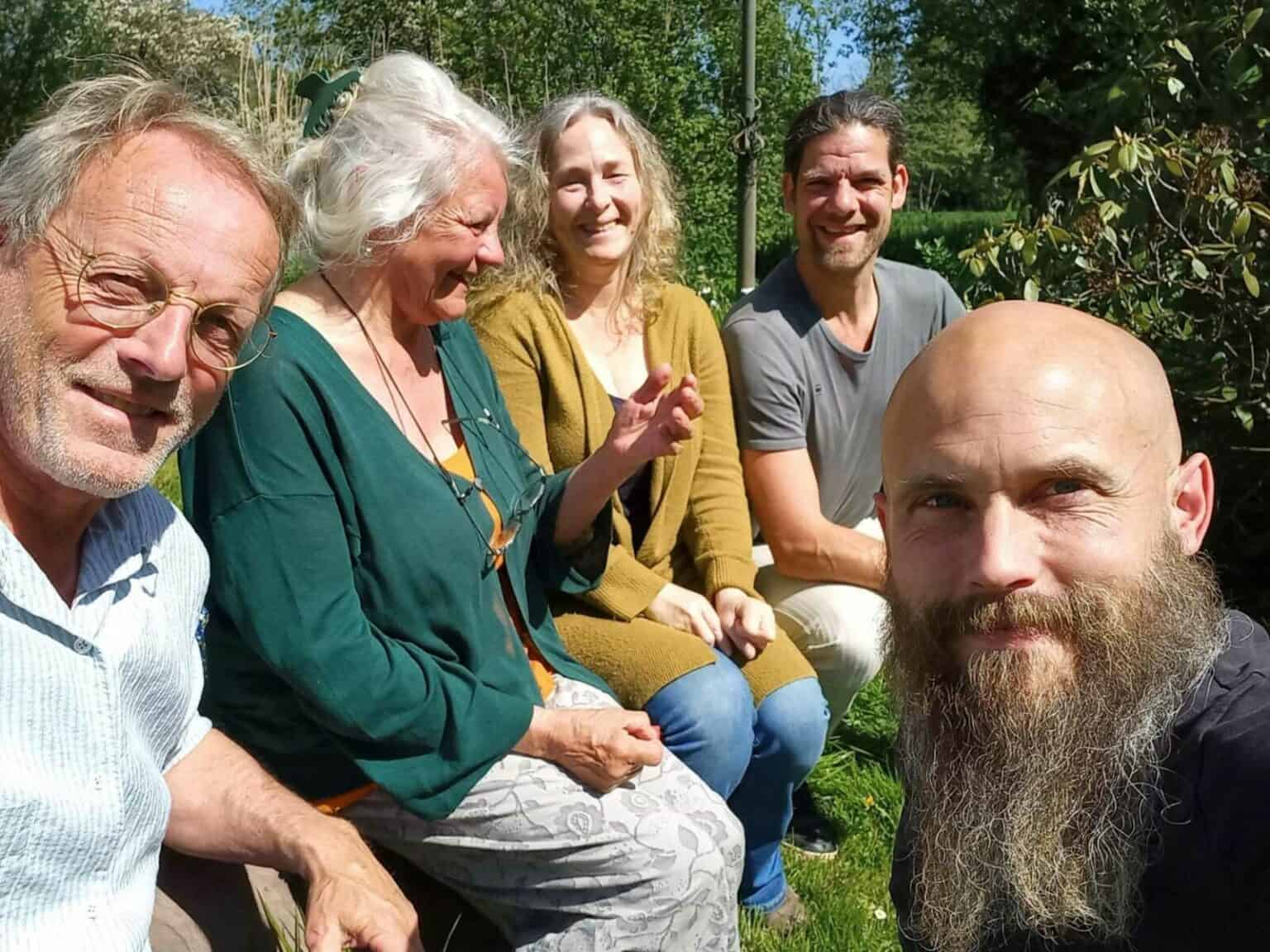 Vijf mensen genieten samen in een tuin op een zonnige dag.